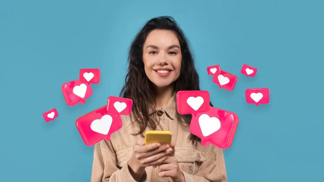 Smiling young woman looking at her phone as pink heart notifications float around her against a teal background, representing social media likes.