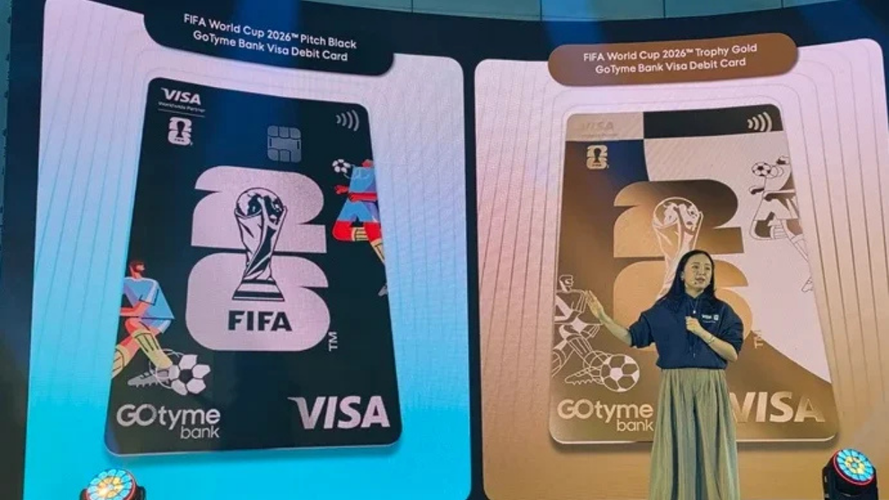 Stage presentation with two oversized FIFA World Cup 2026 GoTyme Bank Visa Debit Card designs (blue left card, gold right card); a woman presenter stands to the right.