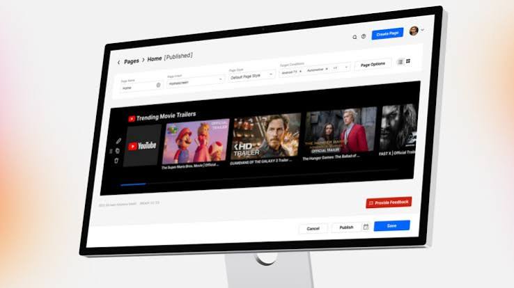 Tilted computer monitor showing a webpage editor with a'Trending Movie Trailers' video thumbnail strip in a dark carousel area.